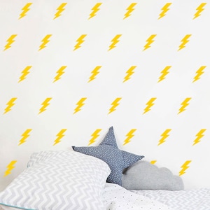 May include: A white wall with a repeating pattern of yellow lightning bolt decals. A bed with a gray and white patterned duvet cover and two pillows is in the foreground.
