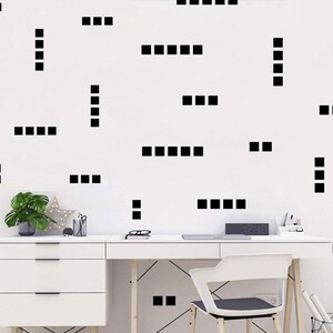 May include: A white wall with black square decals arranged in horizontal and vertical lines. The wall is behind a white desk with a white chair and a black wire basket.