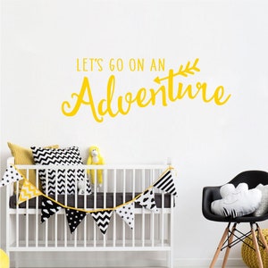 Op de afbeelding: Een wit babybedje met een zwart-witte chevron-gepatenteerde bunting die erboven hangt. De muur achter het babybedje heeft een gele vinyl sticker met de tekst "Let's go on an Adventure" met een pijl en een bladontwerp.