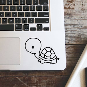 Può includere: Un computer portatile argentato con una tastiera nera e un adesivo di tartaruga bianco e nero sul touchpad.