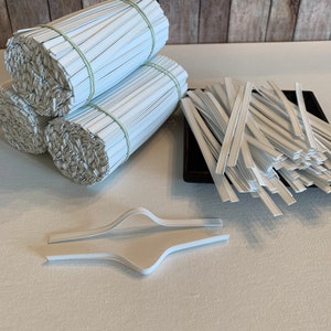 May include: A close-up of white plastic nose wire for face masks. The wire is bundled in three rolls and a pile of individual wires. There are also two white plastic nose wire crimpers.