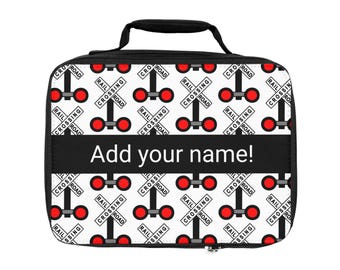 Puede incluir: Una bolsa de almuerzo rectangular con asa y cremallera negras. La bolsa presenta un patrón repetido de señales de cruce de ferrocarril rojas sobre un fondo blanco. Una banda negra en el centro muestra el texto "Add your name!"