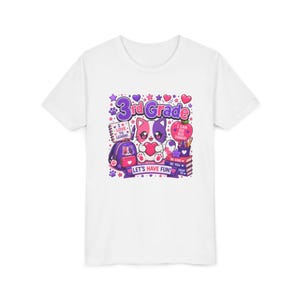 Puede incluir: Una camiseta blanca con un gráfico colorido de un gato sosteniendo un corazón, rodeado de útiles escolares como una mochila, libros y una manzana. El texto dice 3rd Grade, I LOVE TO LEARN, I CAN DO BIG THINGS, BE KIND, BE YOU, DREAM BIG y LET'S HAVE FUN.