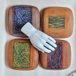 May include: Four square ceramic tiles with a wood-like finish. Each tile has a different design featuring a green and yellow pattern. The tiles are arranged in a square shape.