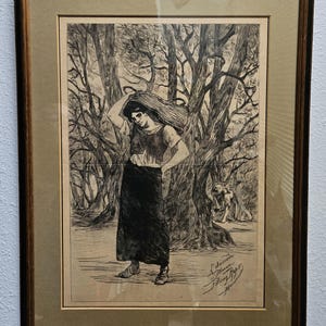 May include: Framed black and white print of a woman in a forest, with a dark skirt and a scarf on her head. The artwork is signed and dated. The frame is dark brown with a light tan mat.