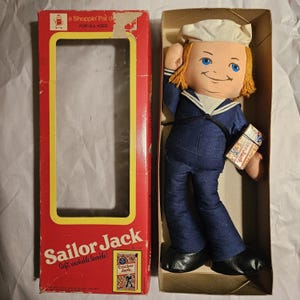 May include: A vintage Sailor Jack doll in a blue sailor suit holding a box of Cracker Jack cereal. The doll is in its original box with the text "a Shoppin' Pal d" and "FOR ALL AGES".