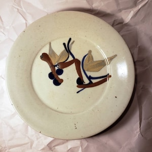 May include: A white ceramic plate with a brown, blue, and yellow design of stylized birds and berries.