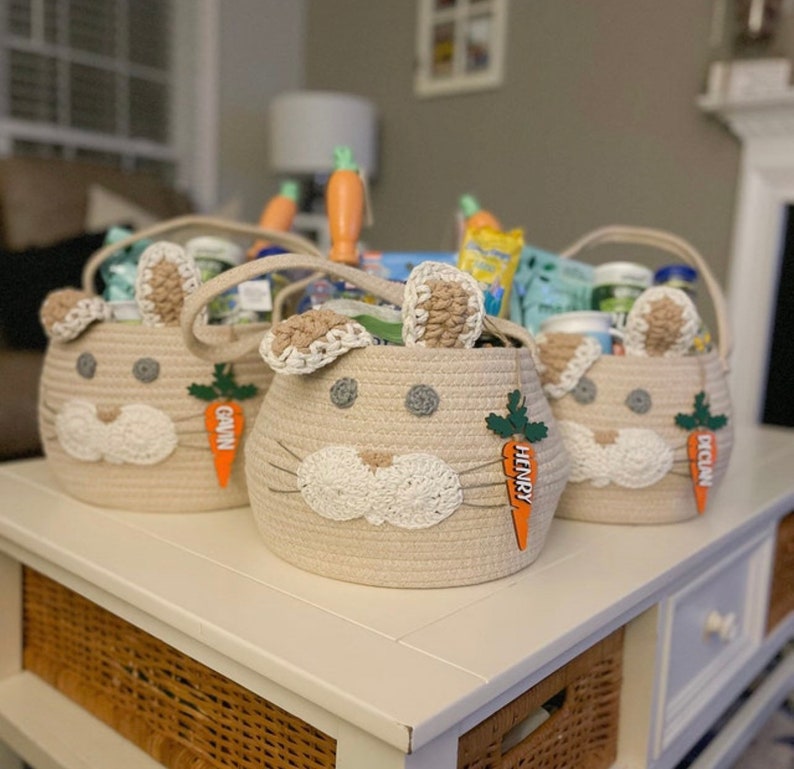 Puede incluir: Tres cestas de conejito beige llenas de golosinas de Pascua. Cada cesta tiene una etiqueta en forma de zanahoria con un nombre: Gavin, Henry y Declan.