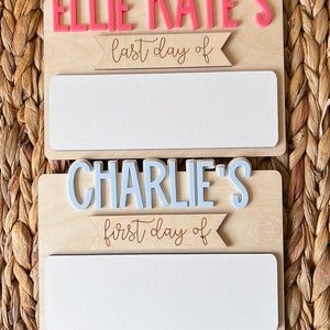 May include: Two wooden signs with white blank spaces for writing. The top sign says "Ellie Kate's last day of" and the bottom sign says "Charlie's first day of".
