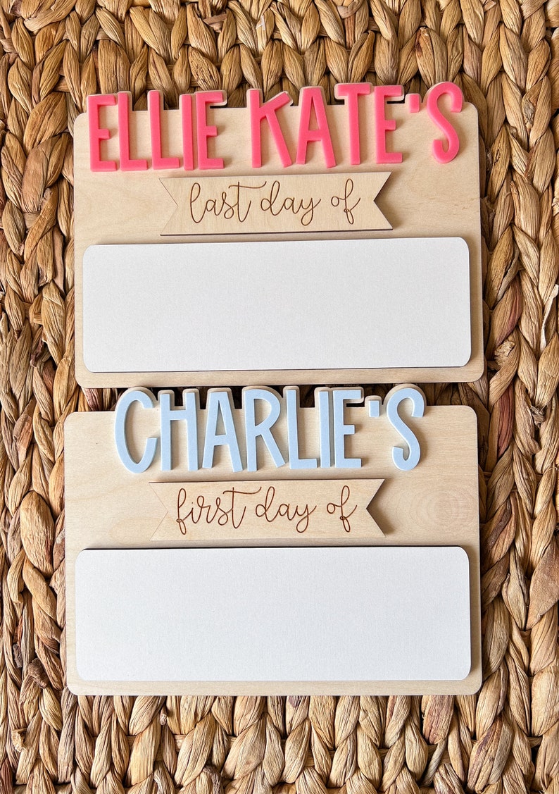 May include: Two wooden signs with white blank spaces for writing. The top sign says "Ellie Kate's last day of" and the bottom sign says "Charlie's first day of".