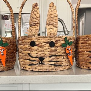 Puede incluir: Tres cestas de Pascua de mimbre marr&oacute;n en forma de conejo con etiquetas en forma de zanahoria naranja. Las etiquetas est&aacute;n etiquetadas como "Zach", "Izzy" y "Essie".