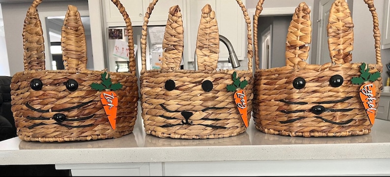 Puede incluir: Tres cestas de Pascua de mimbre marr&oacute;n en forma de conejo con etiquetas en forma de zanahoria naranja. Las etiquetas est&aacute;n etiquetadas como "Zach", "Izzy" y "Essie".