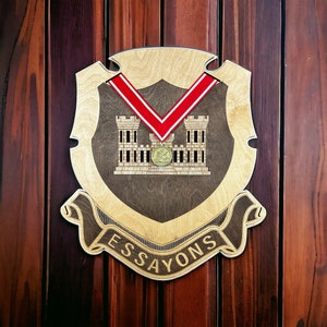 May include: A wooden plaque with a shield shape and a red ribbon. The shield has a brown background and a gold fort with the text "ESSAYONS" on the bottom.
