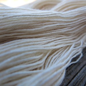 Peut inclure: Un &eacute;cheveau de fil blanc cass&eacute; compos&eacute; de multiples brins fins et torsad&eacute;s assembl&eacute;s. Le fil pr&eacute;sente une texture lisse et mate, dispos&eacute; en une longue boucle continue, mettant en valeur les fibres individuelles et le retors r&eacute;gulier.