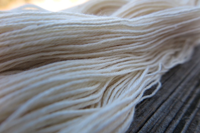 Peut inclure: Un &eacute;cheveau de fil blanc cass&eacute; compos&eacute; de multiples brins fins et torsad&eacute;s assembl&eacute;s. Le fil pr&eacute;sente une texture lisse et mate, dispos&eacute; en une longue boucle continue, mettant en valeur les fibres individuelles et le retors r&eacute;gulier.