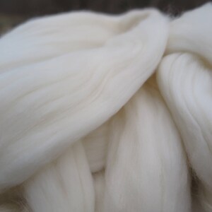 May include: A large, soft mass of unspun white wool roving with a fibrous, combed texture. The material consists of long, parallel strands of clean, off-white animal fiber arranged in a thick, continuous, and fluffy cloud-like formation.