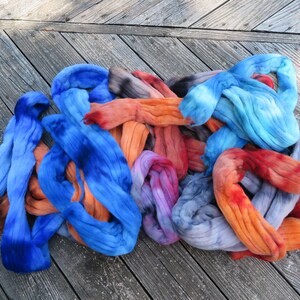 May include: A collection of hand-dyed wool roving fiber in vibrant shades of blue, orange, red, and purple. The soft, unspun textile material is arranged in loose, tangled loops, showcasing a gradient of saturated colors and blended tones.