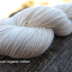 Peut inclure: Un &eacute;cheveau de fil blanc cass&eacute; avec une texture lisse et torsad&eacute;e. Le fil est &eacute;tiquet&eacute; comme American organic cotton. Les fibres sont &eacute;troitement fil&eacute;es en un brin continu, formant une forme arrondie et douce qui souligne la couleur cr&egrave;me.