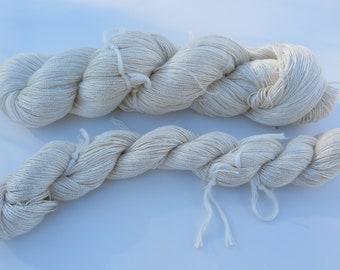 Peut inclure: Deux écheveaux de fil blanc cassé torsadés en longs paquets épais. Le fil présente un aspect texturé et légèrement fibreux avec une couleur naturelle non blanchie. Chaque écheveau est fixé par de petits liens blancs pour maintenir sa forme.