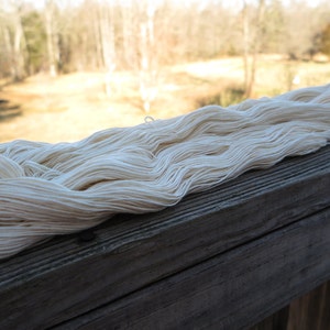 Peut inclure: Un long &eacute;cheveau continu de fil blanc cass&eacute; pr&eacute;sentant une texture douce et torsad&eacute;e. Le fil est compos&eacute; de multiples brins fins individuels regroup&eacute;s en une boucle l&acirc;che et allong&eacute;e, mettant en valeur une teinte naturelle, cr&egrave;me et neutre.