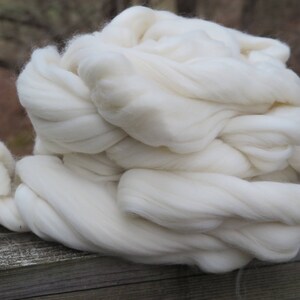 May include: A large, fluffy bundle of unspun white wool roving. The material consists of long, soft, and continuous fibers that are loosely twisted together, creating a voluminous and cloud-like texture with a bright, clean, and solid white color.