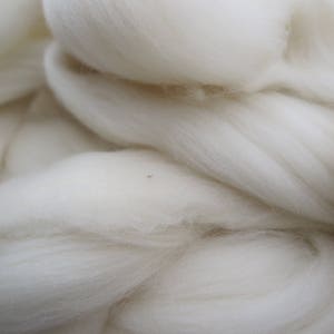 May include: A large, dense mass of unspun white wool fiber. The material features a soft, fluffy, and fibrous texture with long, continuous strands layered and intertwined to create a voluminous, cloud-like appearance with a bright white color.