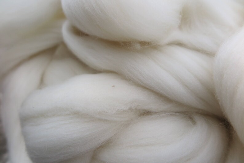 May include: A large, dense mass of unspun white wool fiber. The material features a soft, fluffy, and fibrous texture with long, continuous strands layered and intertwined to create a voluminous, cloud-like appearance with a bright white color.