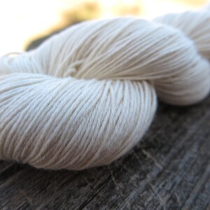 Peut inclure: Un &eacute;cheveau de fil couleur blanc cass&eacute; pr&eacute;sentant une texture torsad&eacute;e lisse &agrave; plusieurs brins. Le fil est enroul&eacute; en une longue boucle continue avec des brins individuels visibles qui cr&eacute;ent un aspect uniforme sur toute la longueur.
