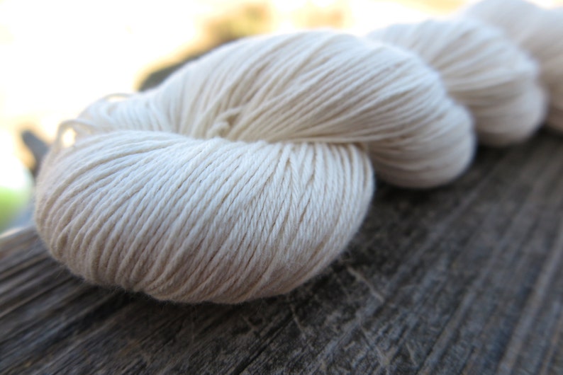 Peut inclure: Un &eacute;cheveau de fil couleur blanc cass&eacute; pr&eacute;sentant une texture torsad&eacute;e lisse &agrave; plusieurs brins. Le fil est enroul&eacute; en une longue boucle continue avec des brins individuels visibles qui cr&eacute;ent un aspect uniforme sur toute la longueur.