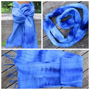 May include: A long, rectangular scarf featuring a gradient of blue tones ranging from light sky blue to deep navy. The fabric displays a textured, felted appearance with horizontal stripes and fringe detailing at the ends of the scarf.