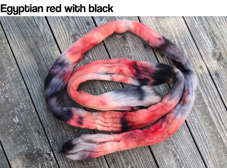 May include: A coiled length of hand-dyed yarn featuring a variegated color palette of vibrant red, soft pink, and deep black tones. The text "Egyptian red with black" is printed in the upper left corner of the image, describing the colorway.