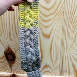 May include: A gray and yellow knitted bracelet with a wooden button that says "Handmade with Love".