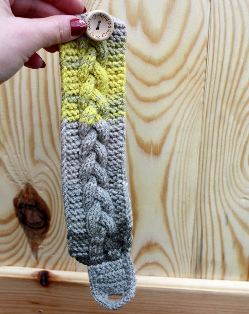 May include: A gray and yellow knitted bracelet with a wooden button that says "Handmade with Love".