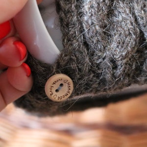May include: A close-up of a brown knitted mug cozy with a wooden button that says "Handmade with love" in cursive.