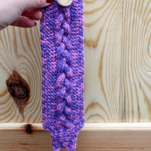 May include: Purple and pink knitted wrist warmer with a wooden button that says "Handmade with love".