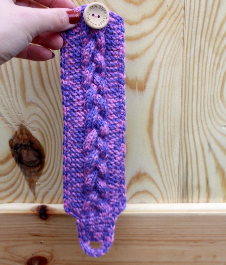May include: Purple and pink knitted wrist warmer with a wooden button that says "Handmade with love".