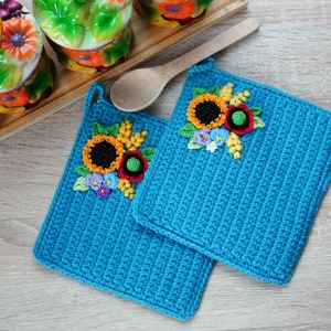 May include: Two blue crocheted pot holders with sunflower and flower embroidery. The pot holders have a loop for hanging.