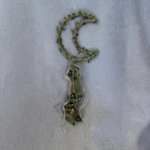 May include: A crescent moon-shaped wreath made of twine and green leaves with a small bell hanging from the bottom.