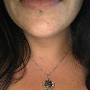 May include: A silver chain necklace with a round pendant featuring a green, brown, and black stone set in a silver filigree design.