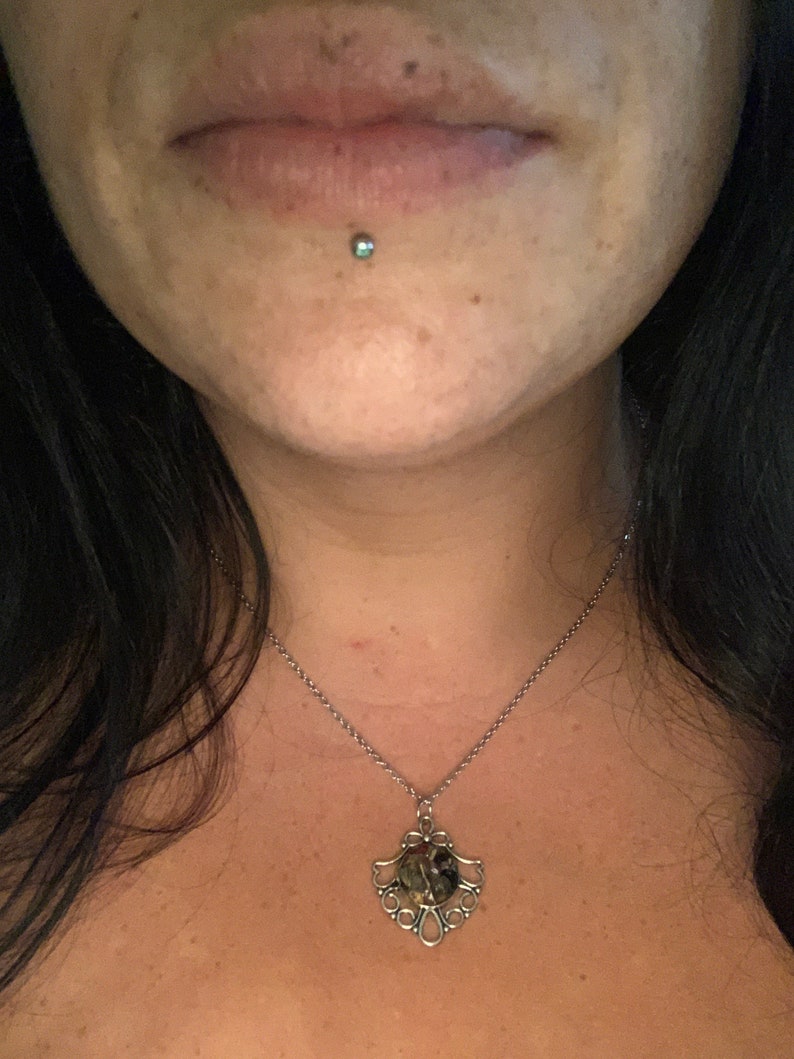 May include: A silver chain necklace with a round pendant featuring a green, brown, and black stone set in a silver filigree design.