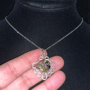 May include: A silver chain necklace with a silver pendant featuring a round, clear resin cabochon filled with colorful, iridescent flakes.