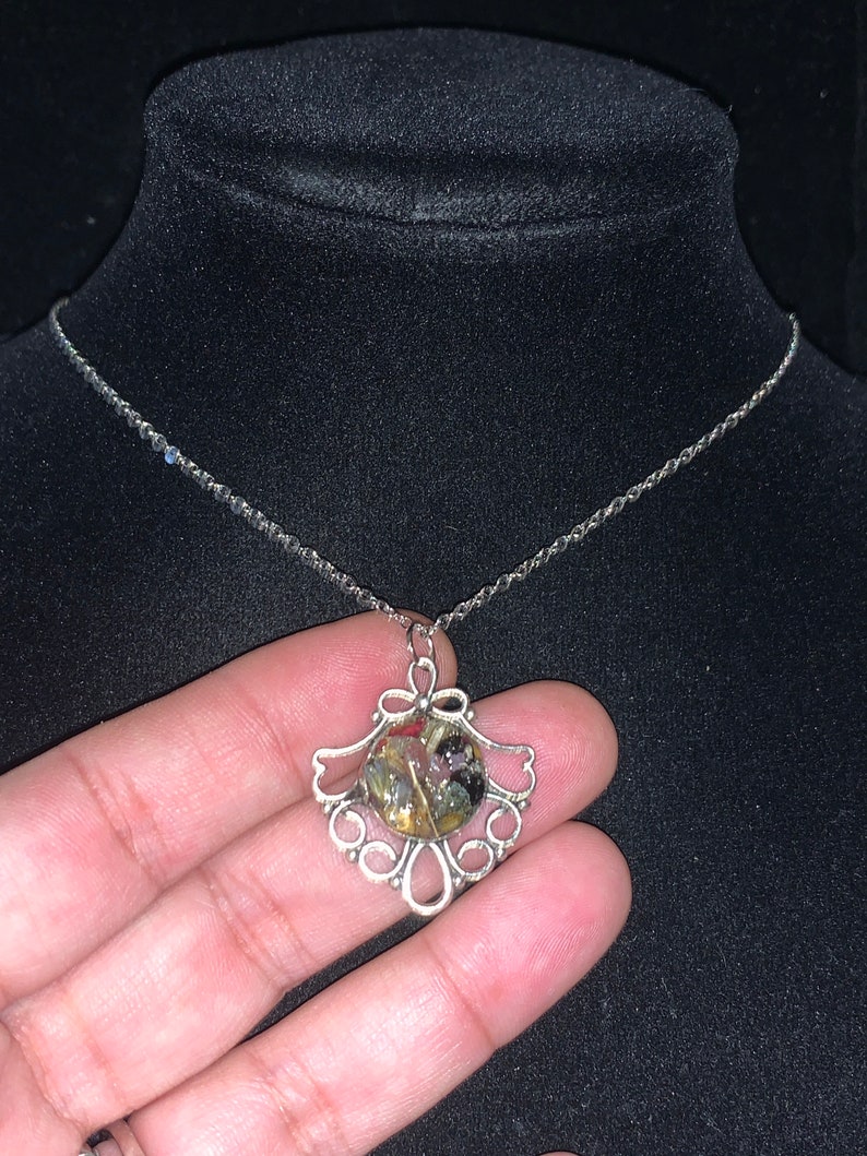 May include: A silver chain necklace with a silver pendant featuring a round, clear resin cabochon filled with colorful, iridescent flakes.