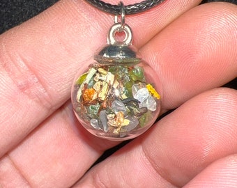 May include: A silver necklace with a clear glass orb pendant filled with various small stones and crystals, including green, brown, and white stones.