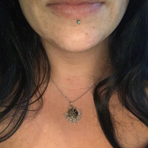 May include: A silver chain necklace with a silver pendant featuring a round, multi-colored stone surrounded by a decorative design.