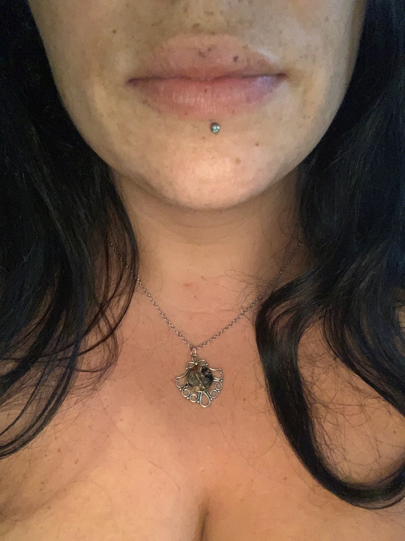 May include: A silver chain necklace with a silver pendant featuring a round, multi-colored stone surrounded by a decorative design.