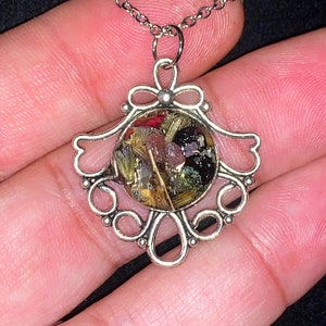 May include: A silver necklace with a delicate filigree pendant. The pendant features a round glass dome filled with dried flowers and herbs.