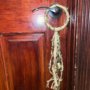 May include: A brown door with a door handle and a decorative wreath with bells hanging from it.