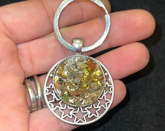May include: Silver keychain with a round charm featuring a mix of gold, green, and clear stones set in a silver starburst design.