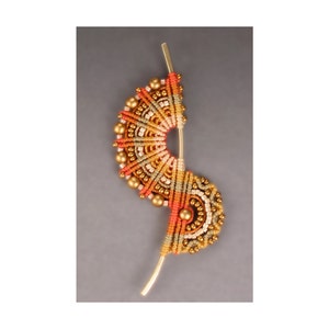 May include: A gold and orange beaded jewelry piece with a spiral design. The piece is made with a variety of beads and is attached to a gold wire.