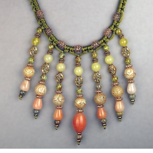 May include: A green cord necklace with multiple strands of beads. The beads are a mix of light green, peach, and orange colors. The necklace has a tassel-like design with the beads hanging from the cord.